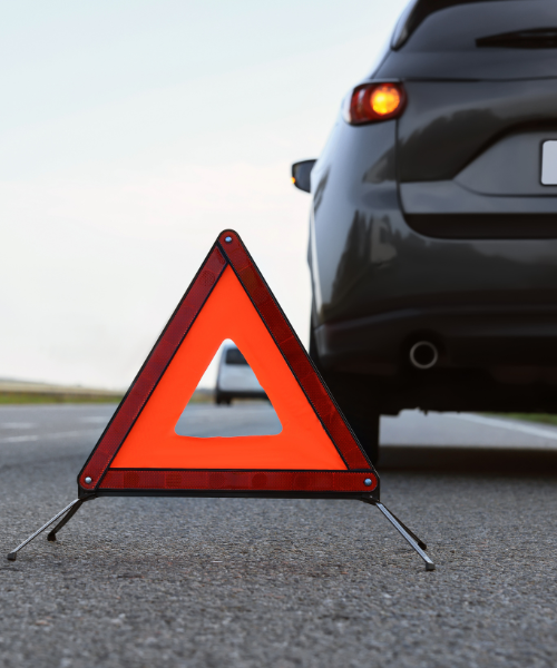 A triangle sign sitting on the side of a road next to a car